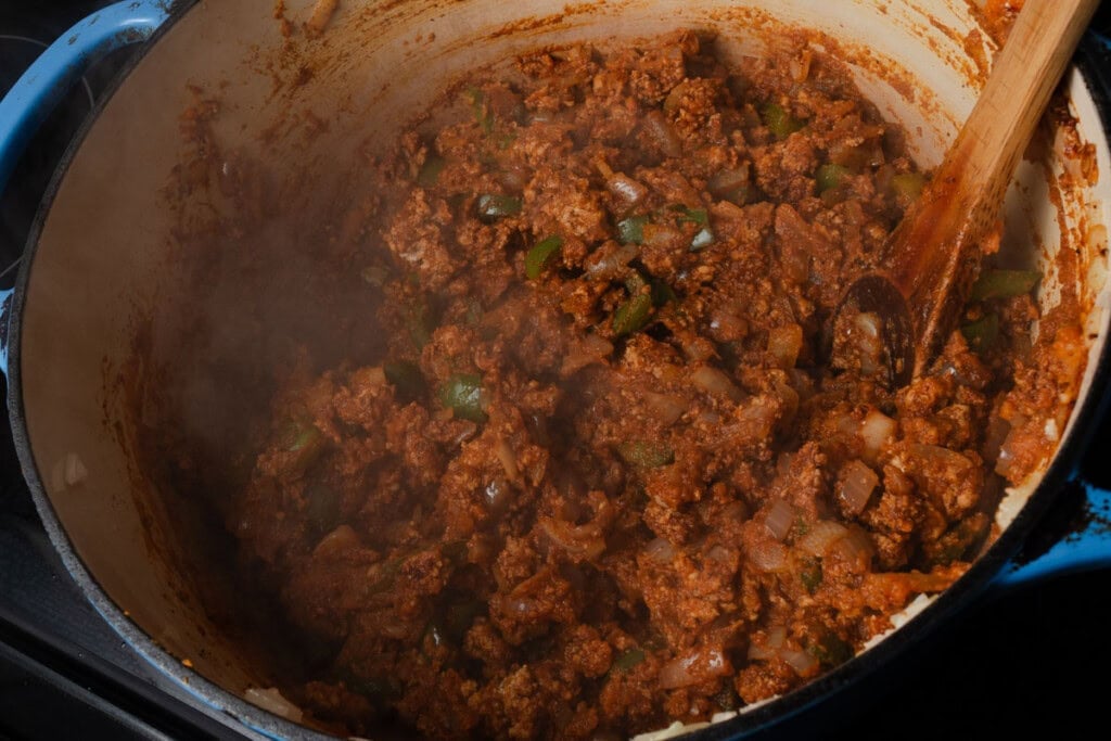 Stirring peppers, onions, garlic, ground turkey, pumpkin puree, and chili spices in a dutch oven.