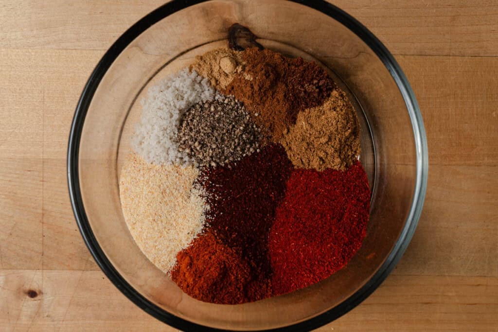 Chili powder, paprika, cayenne, garlic, cumin salt, pepper, cinnamon, cloves, nutmeg, and ginger in a bowl.