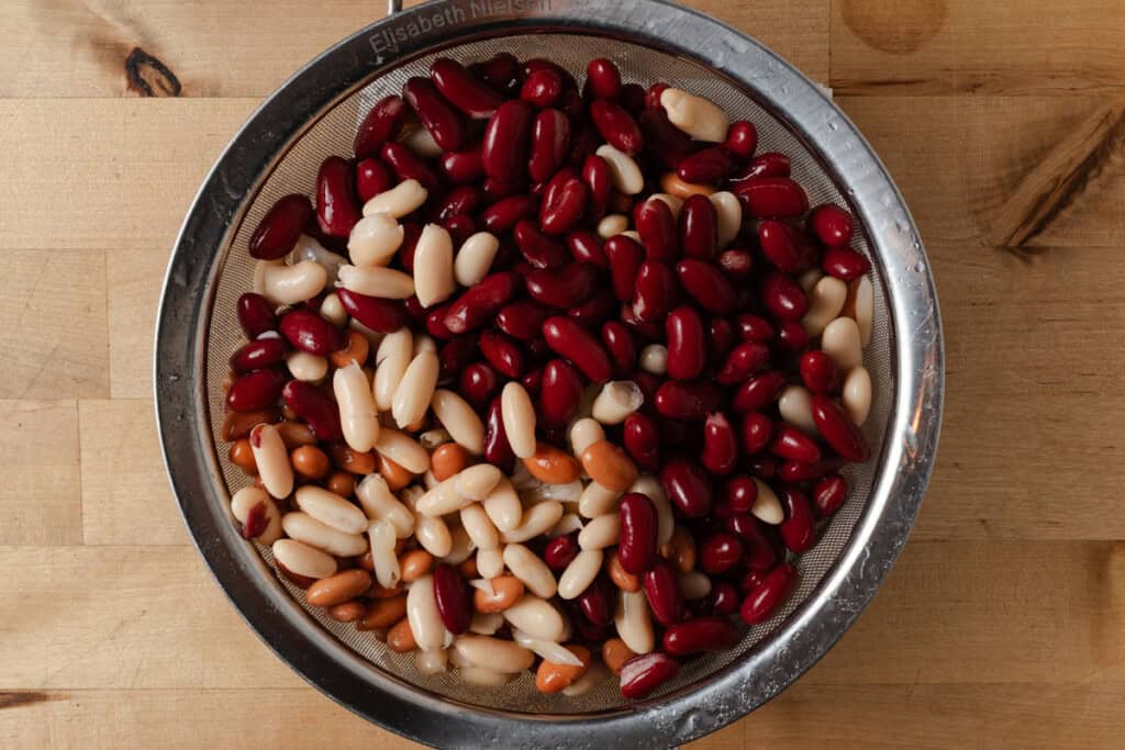 Rinsed and drained pinto beans, cannellini beans, and red kidney beans in a mesh strainer.