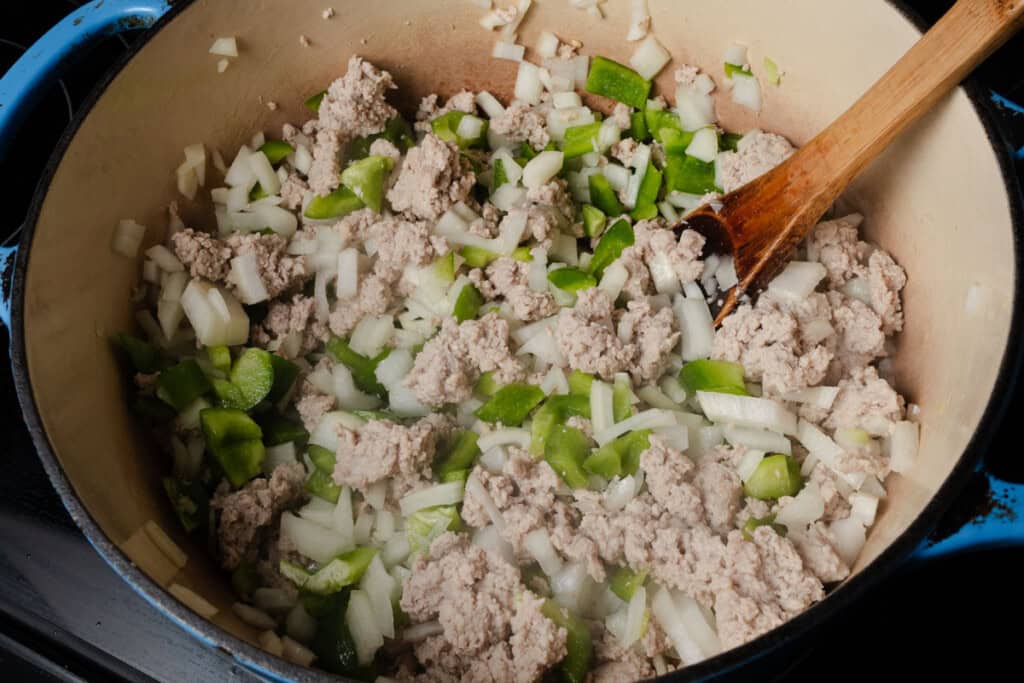 Stirring peppers, onions, garlic, and ground turkey in a Dutch oven.