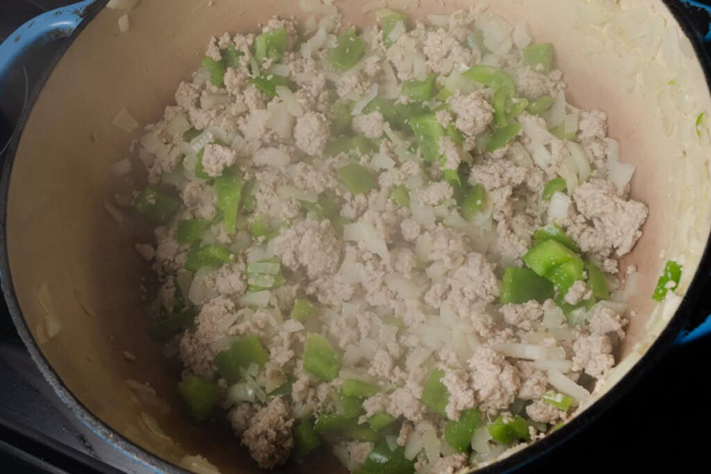 Stirring peppers, onions, garlic, and ground turkey in a dutch oven.
