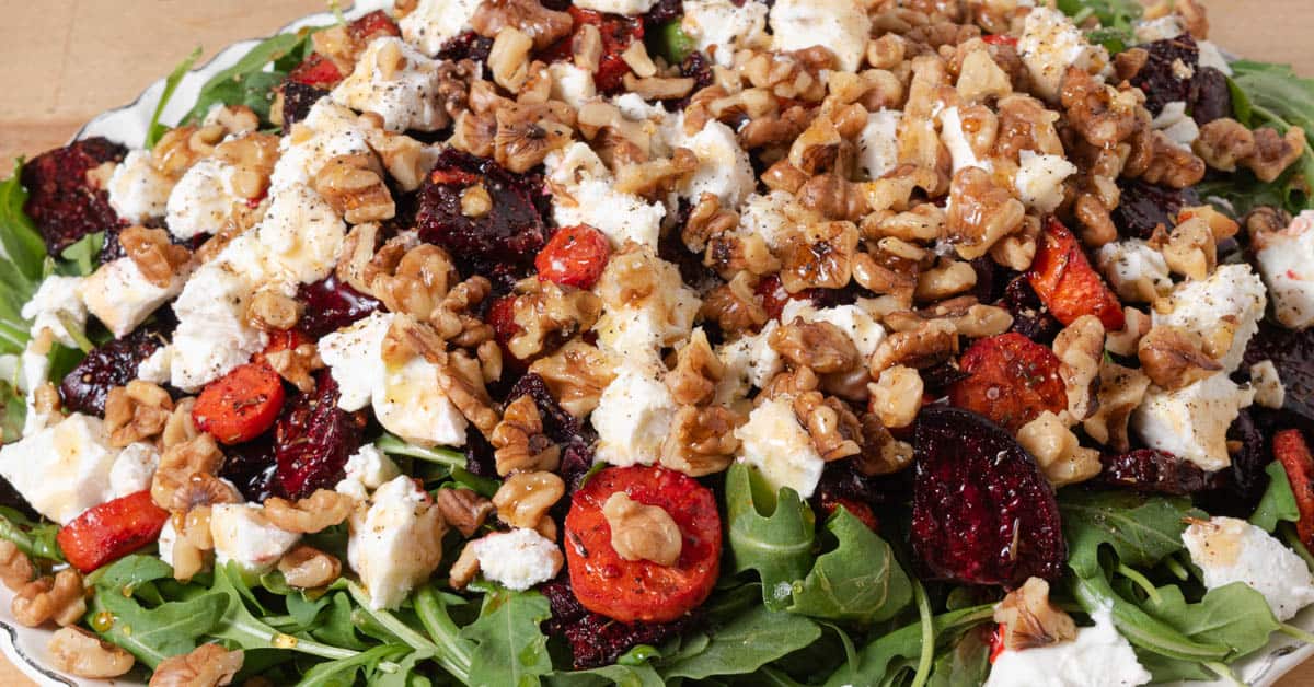 A salad with arugula, roasted beets and carrots, goat cheese, toasted walnuts, and hot honey.