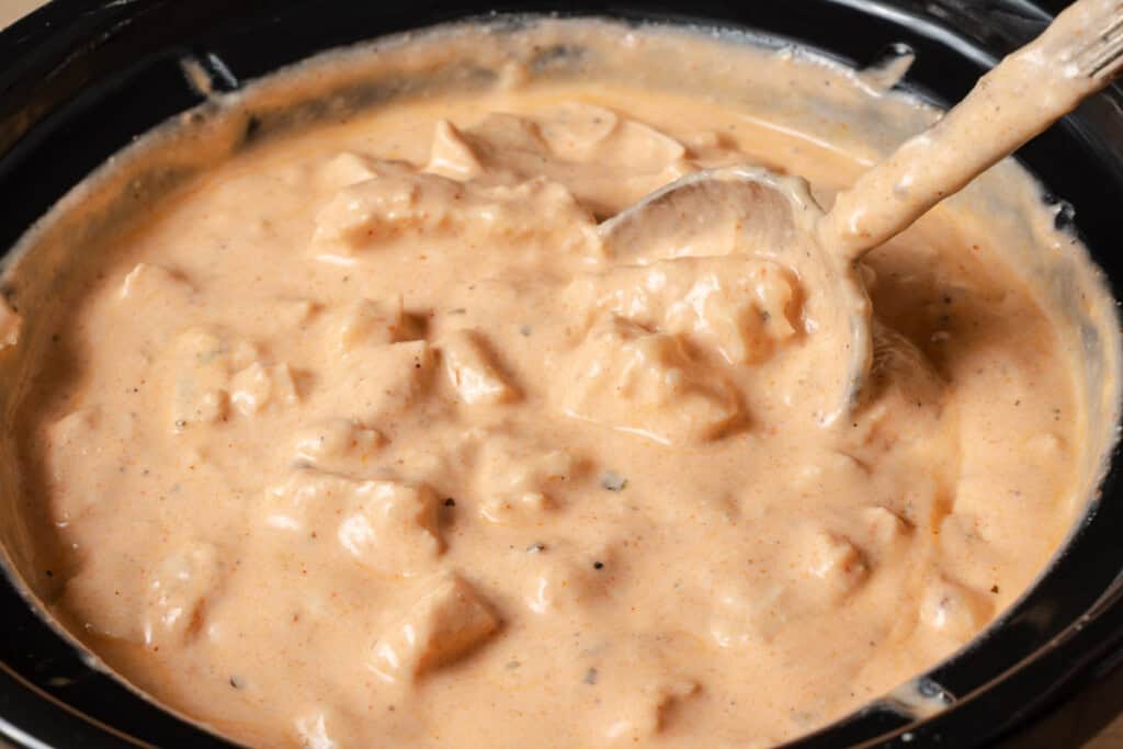 Stirring the pepper jack cheese into slow cooker buffalo chicken dip.