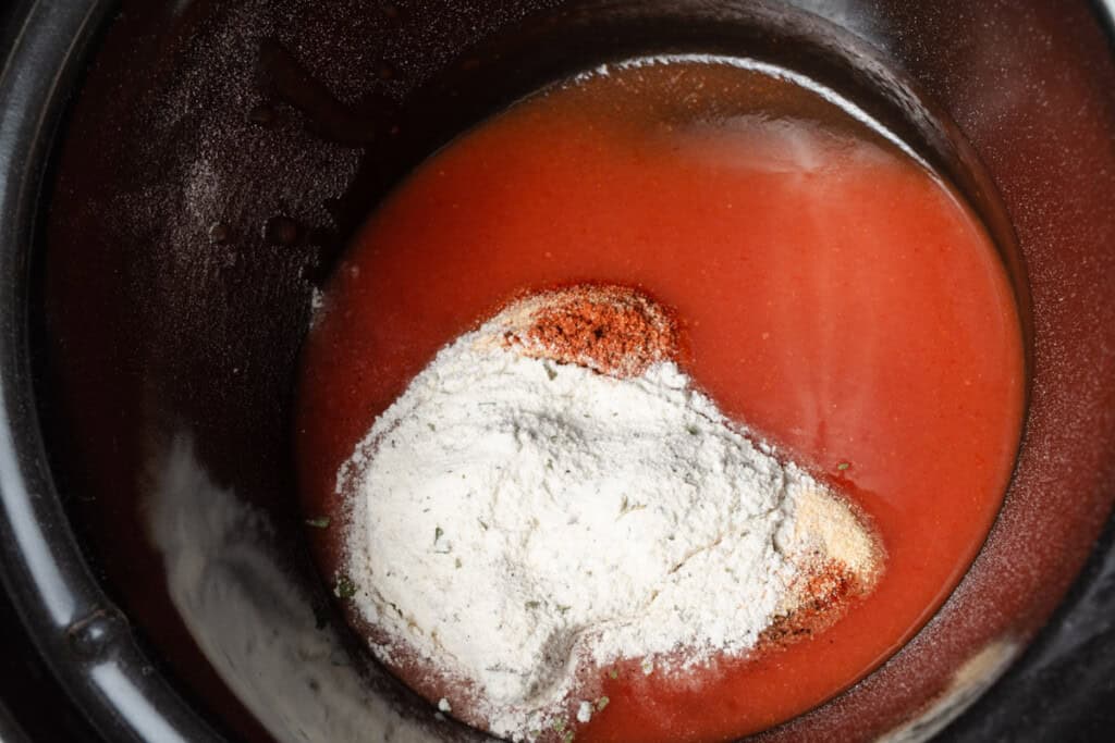 Frank's hot sauce, ranch seasoning, garlic, cayenne, and pepper in a slow cooker insert.