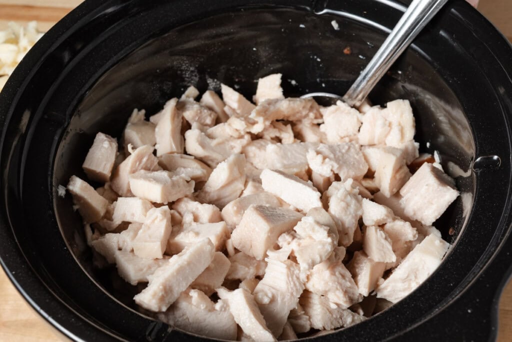 Adding cooked chicken breast to Frank's hot sauce and ranch seasoning in a slow cooker insert.