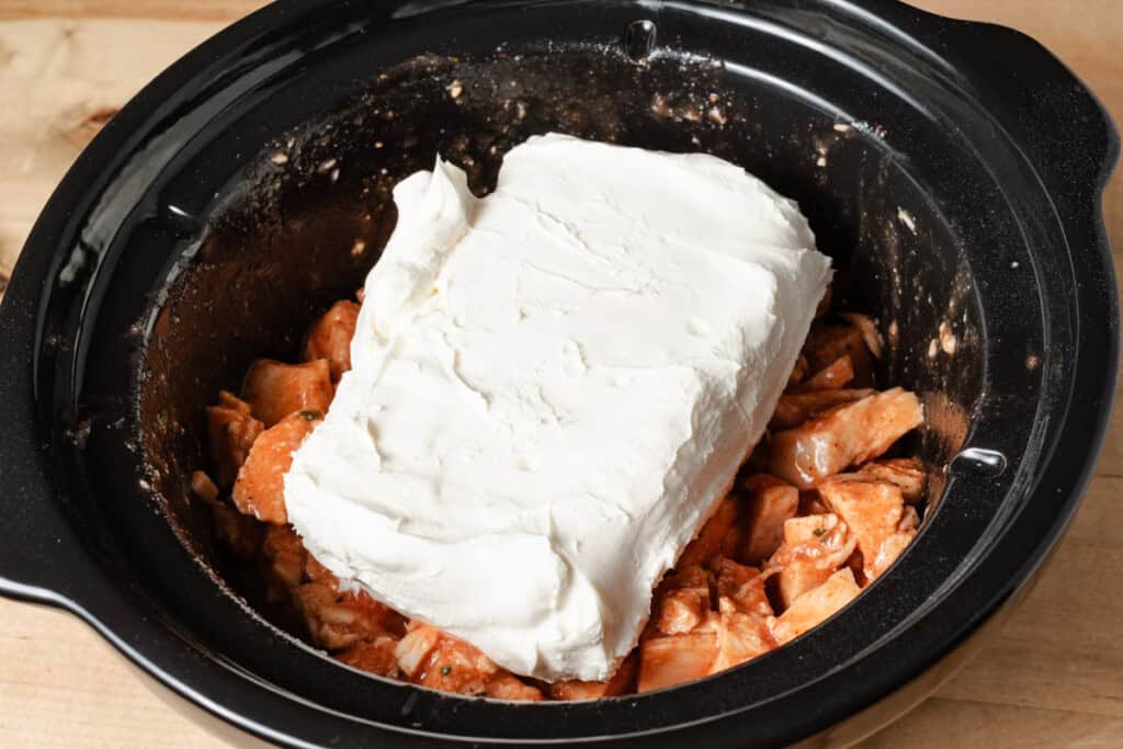 Chicken breast, ranch seasoning, Frank's hot sauce, and cream cheese in a slow cooker insert.