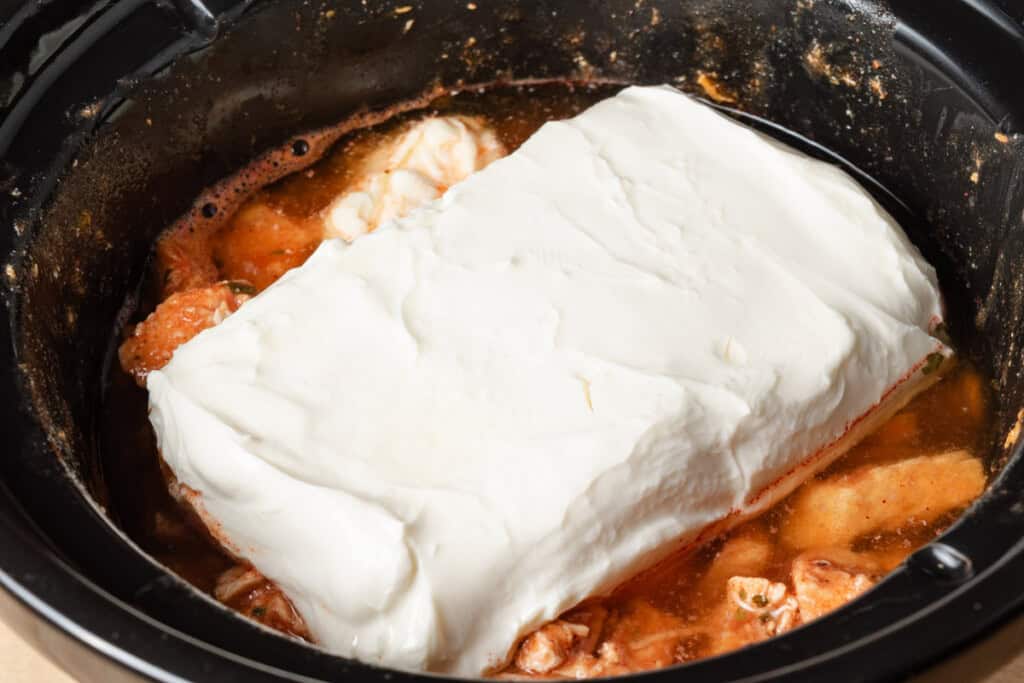 Chicken breast, ranch seasoning, Frank's hot sauce, and cream cheese in a crock pot after being slow cooked.
