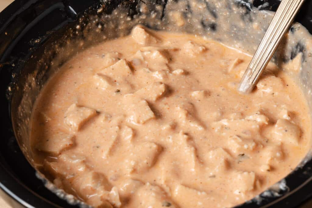 Stirring cream cheese into slow cooked buffalo chicken dip.