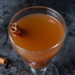 A glass of hot mulled apple cider with a cinnamon stick.