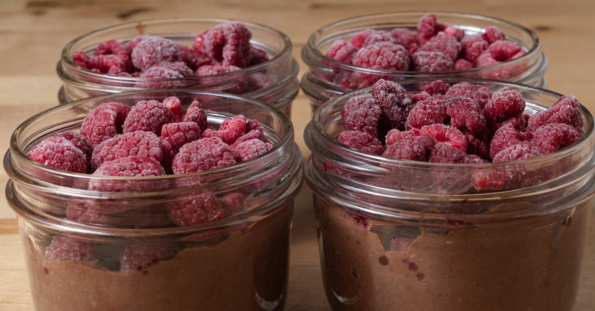 Mason jars full of chocolate chia pudding and topped with frozen raspberries.