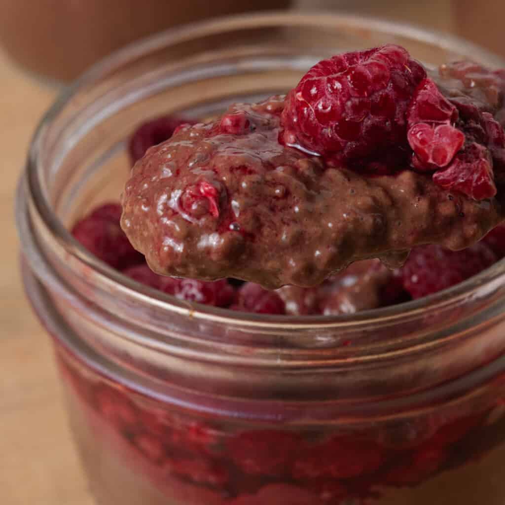 Jars of chocolate chia pudding topped with jammy raspberries.