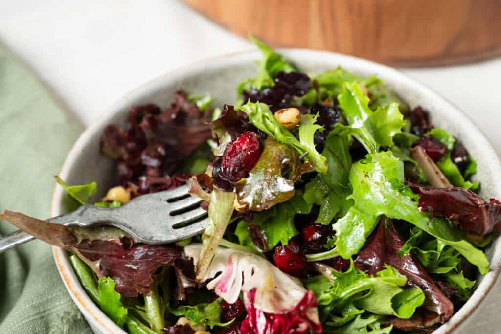 A forkful of cranberry walnut salad in a bowl of green salad.