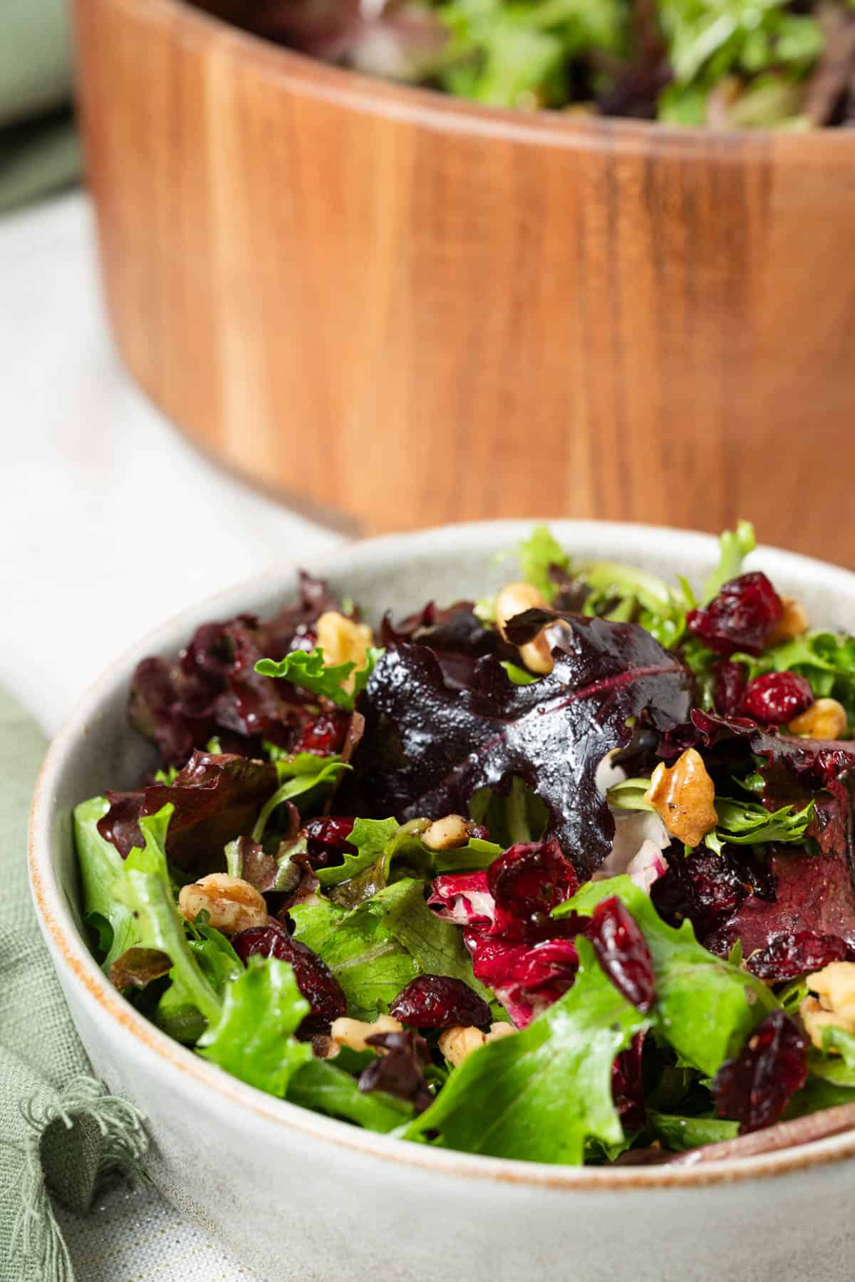 A bowl of salad greens with dried cranberries, walnuts, and balsamic vinaigrette sitting on a table.