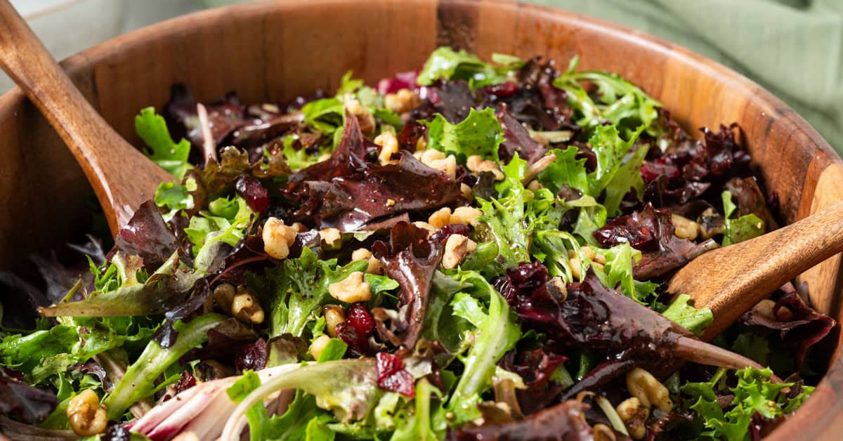 A bowl of mixed greens with dried cranberries and walnuts.