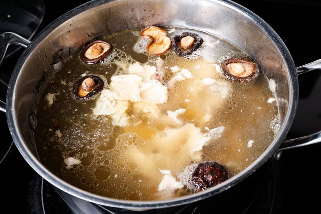 A chicken carcass simmering in a stock pot with mushrooms and other aromatics.