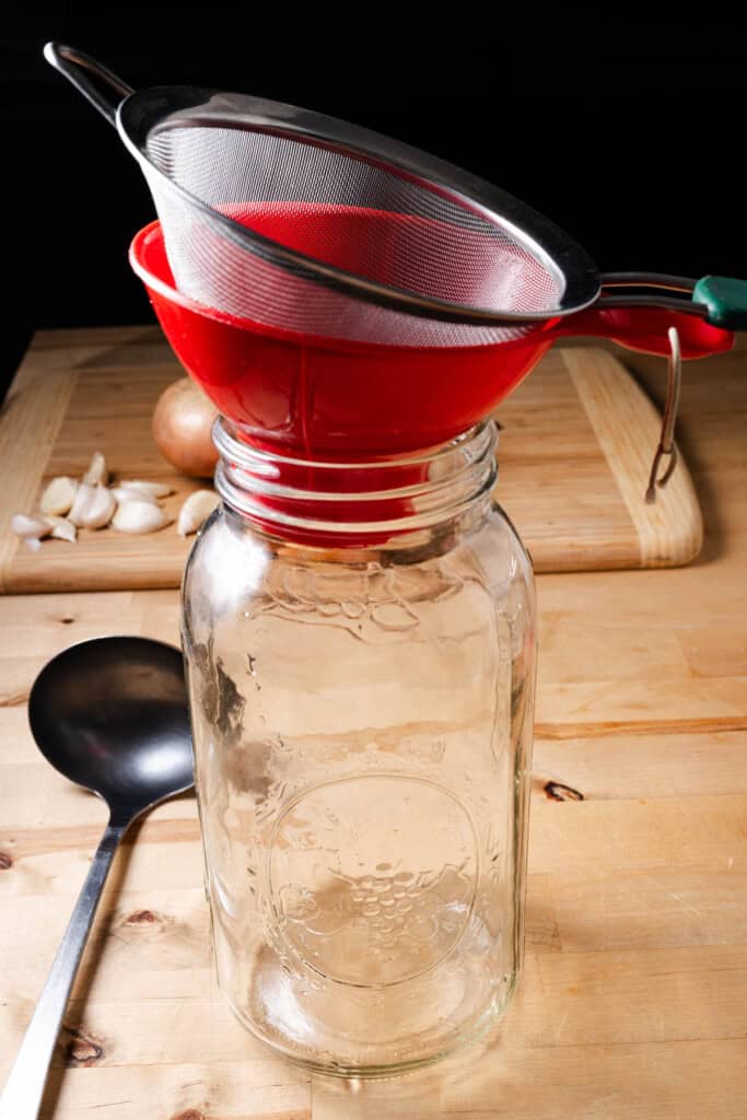 A half gallon mason jar with a wide mouth canning funnel in the top and a fine mesh sieve on top.