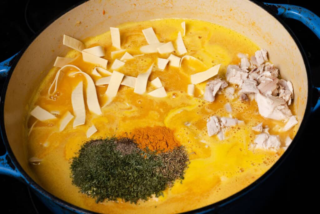Adding egg noodles, cooked chicken, dill, thyme, parsley, turmeric, salt, and pepper to a pot soup broth.