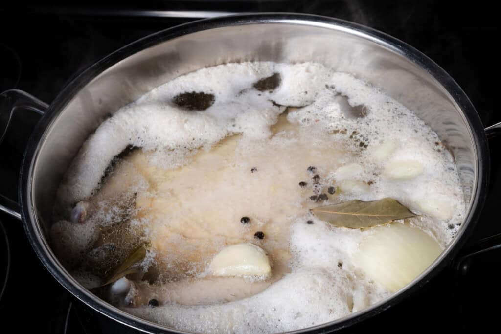 Bringing a stockpot with water and chicken to a simmer.
