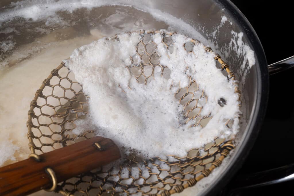 Using a spider skimmer to skim the foam off of poached chicken.