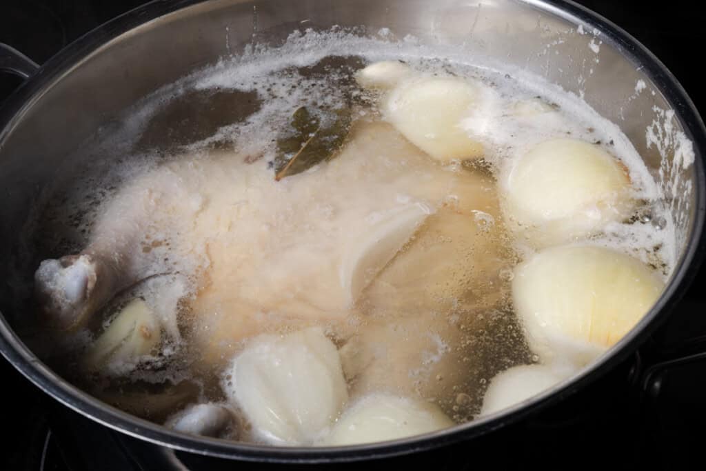 A whole chicken simmering in a stockpot.