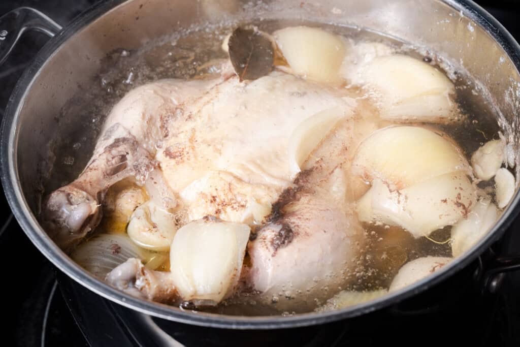 A whole chicken simmering in a stockpot.