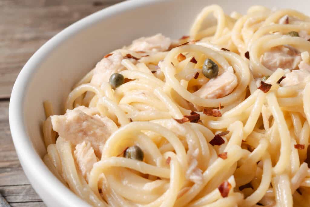 A bowl of tuna butter spaghetti topped with capers and crushed pepper flakes.