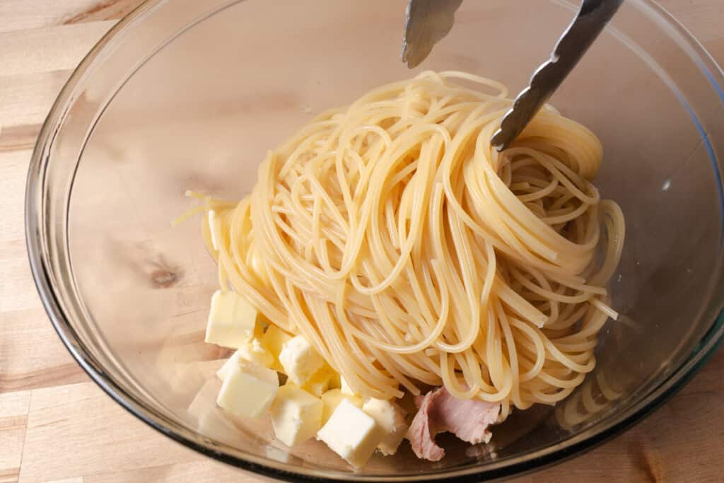 Using tongs to add hot spaghetti noodles to a bowl of tuna and butter.