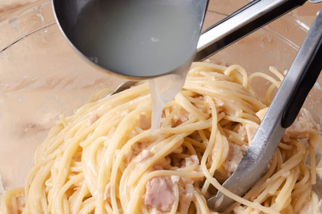 Adding starchy pasta cooking water to tuna butter spaghetti to create an emulsified sauce.