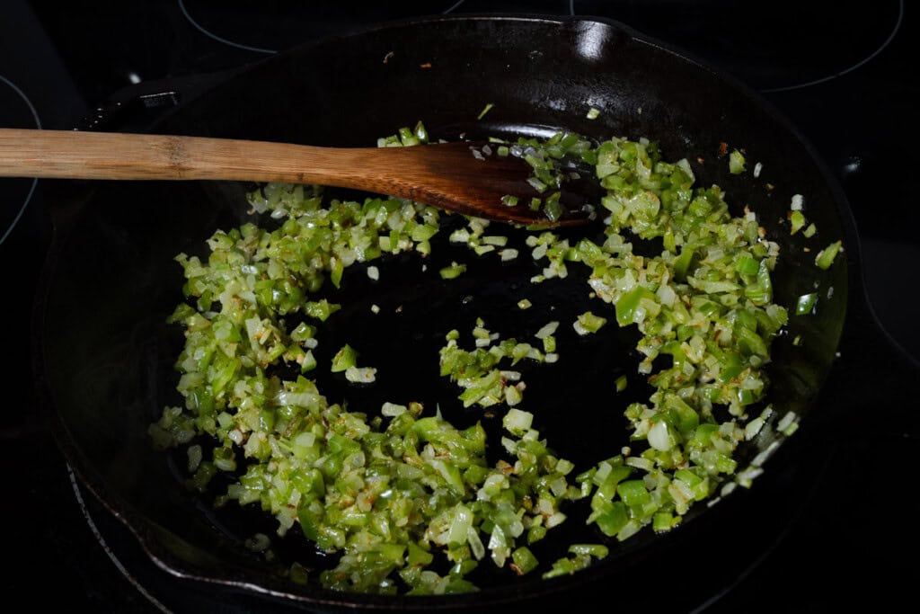 Cooking diced celery, bell peppers, and yellow onions in a cast iron skillet.
