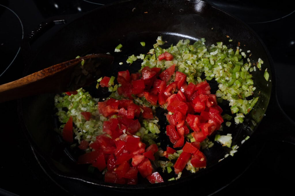 Adding tomatoes and garlic to trinity in a skillet.