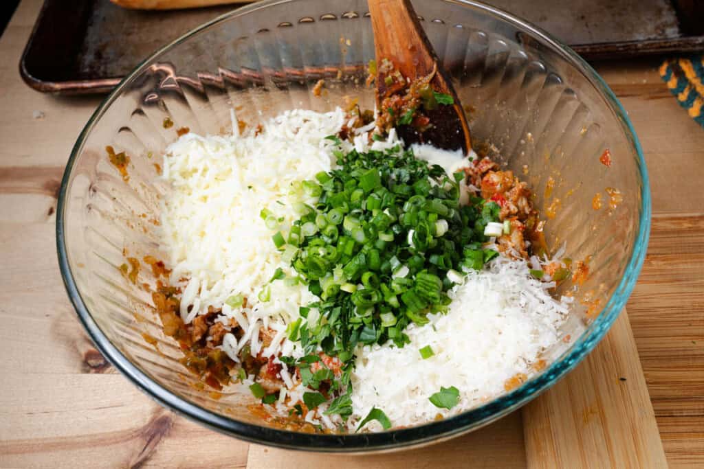 Adding cheeses, herbs, and mayonnaise to a bowl of creole crawfish.