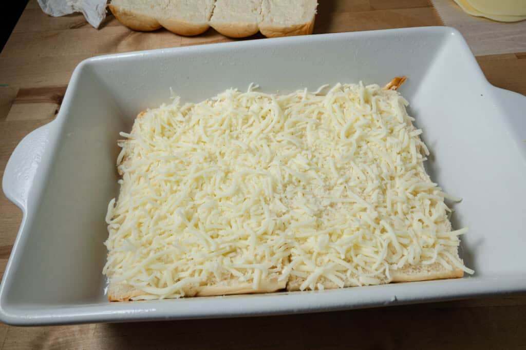 Layering shredded mozzarella on a pan of pizza sliders.