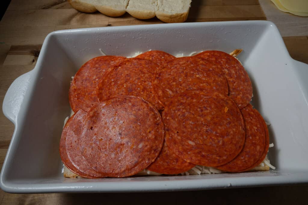 Layering pepperonis on a pan of pizza sliders.