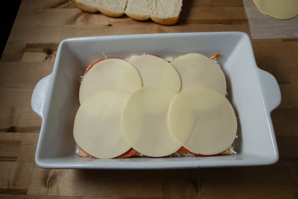 Layering provolone on a pan of pizza sliders.
