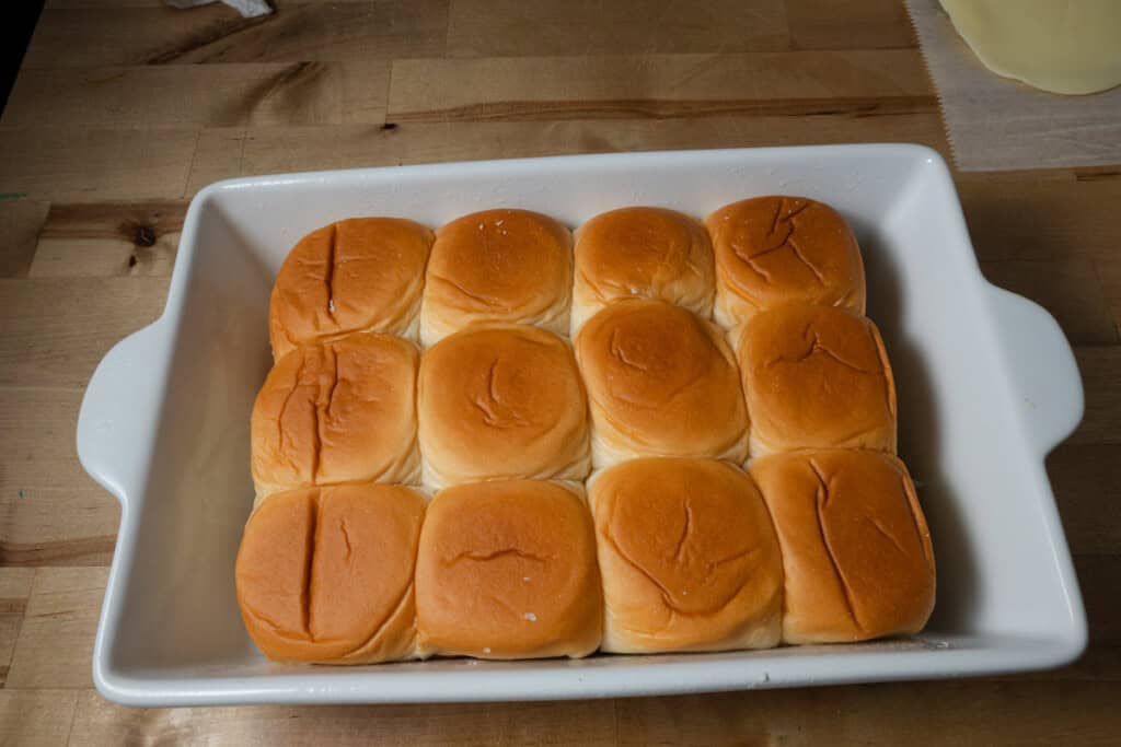 Placing the top buns on a pan of pizza sliders.
