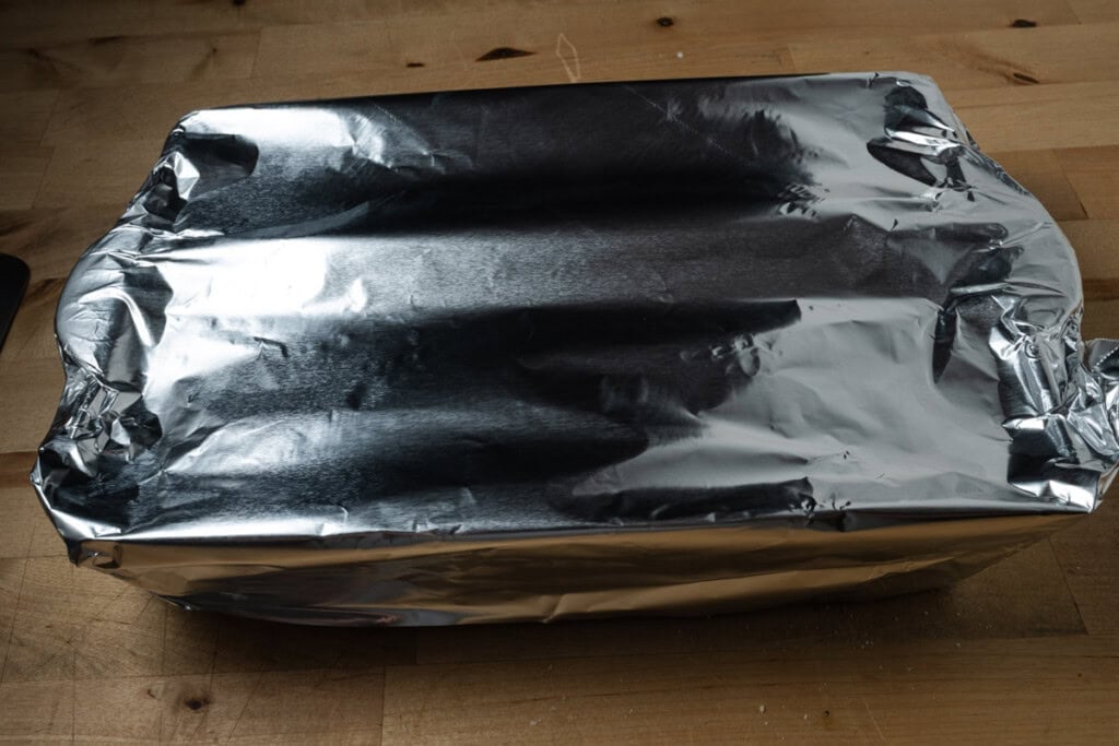 Covering pizza sliders with aluminum foil for baking.