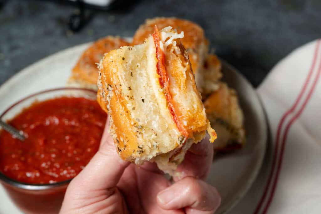 A hand holding a pepperoni pizza slider.