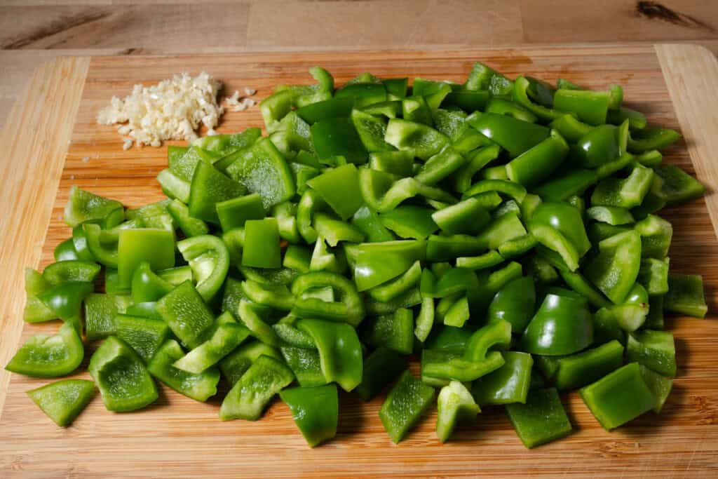 Cut bell peppers and minced onions on a cutting board.