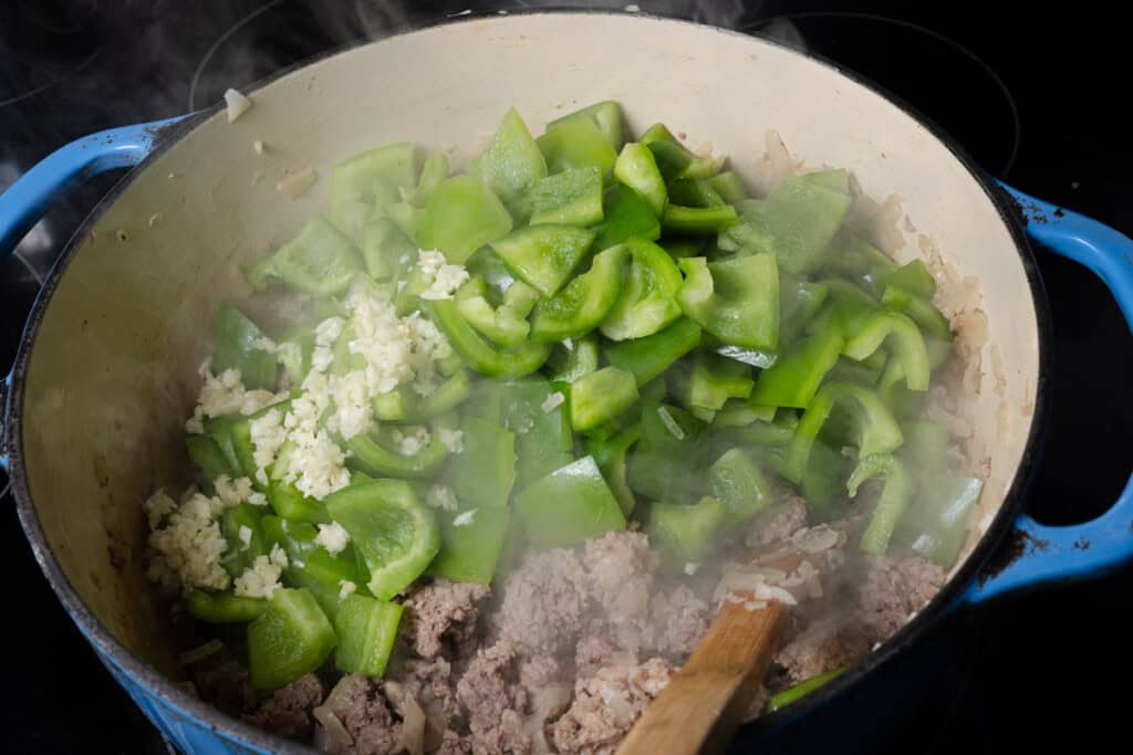 Adding bell peppers and minced onions to a Dutch oven.