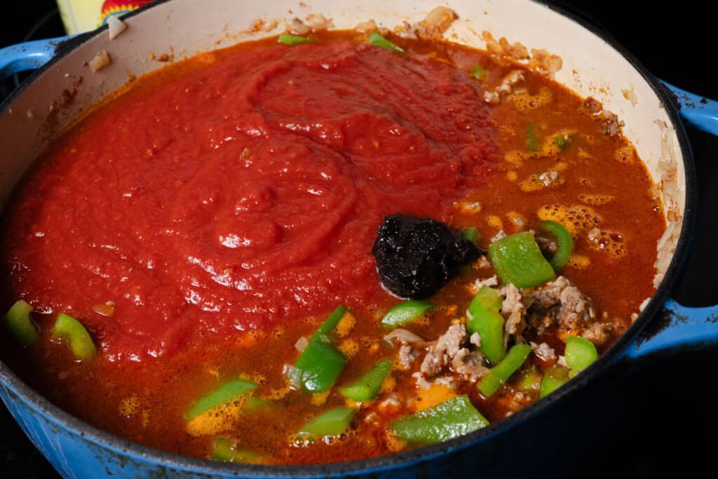 Adding crushed tomatoes, water, and beef bullion to stuffed pepper soup.