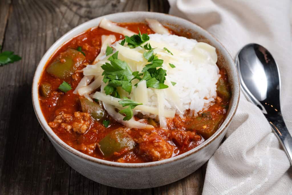 A bowl of stuffed pepper soup with rice, cheese, and parsley.
