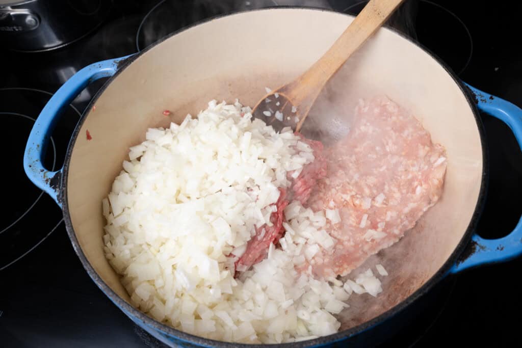 Cooking onions, Italian sausage, and ground beef in a Dutch oven.