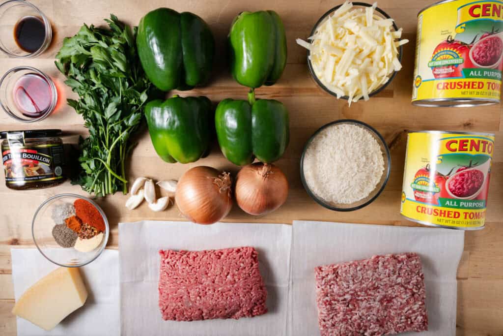 Italian sausage, ground beef, onions, garlic, bell peppers, crushed tomatoes, beef bullion, spices, red wine vinegar, worchestershire sauce, parsley, cheeses, and rice on a countertop for making soup.
