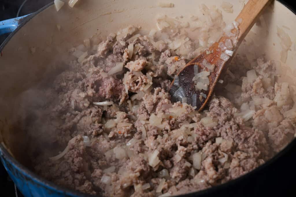 Cooking diced onions, Italian sausge, and ground beef in a Dutch oven.
