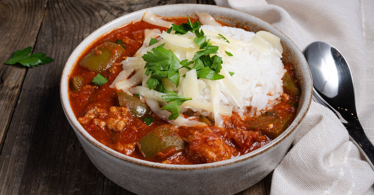 A bowl of homemade stuffed pepper soup topped with rice, cheese, and parsley.