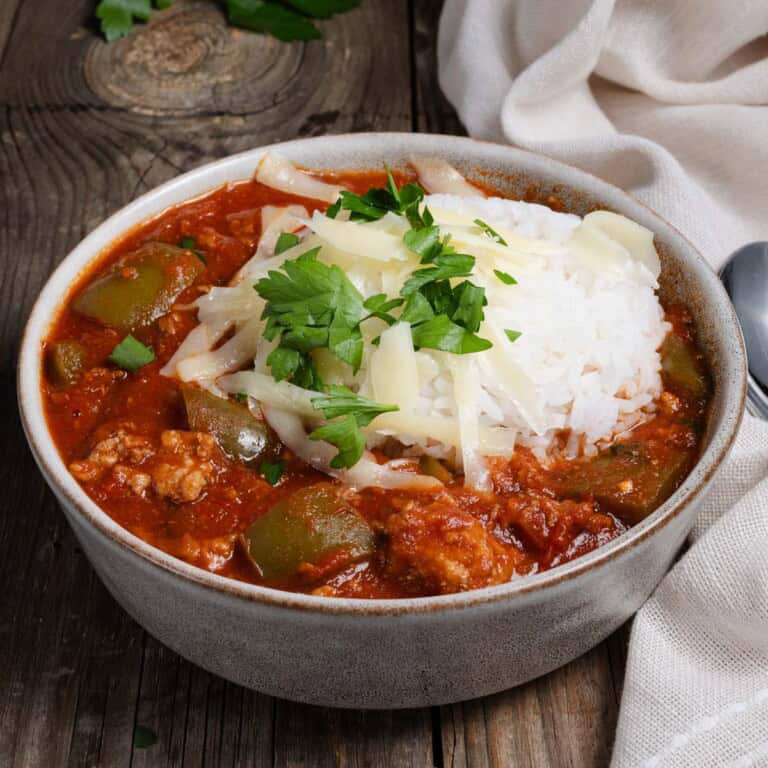 A bowl of stuffed pepper soup with rice, cheese, and parsley.