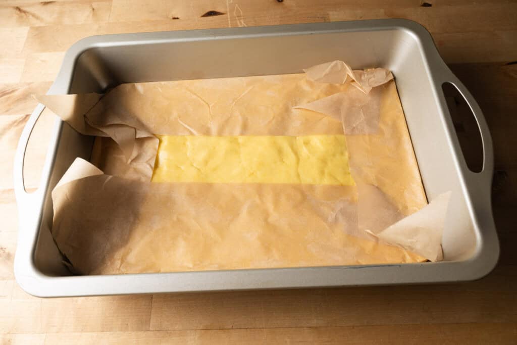Pressing chess bar crust into a parchment lined cake pan.