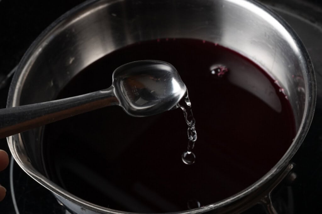 Adding orange blossom water to a pot of pomegranate juice and sugar.