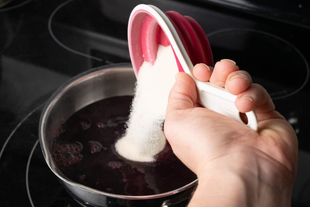 Pouring sugar into a pot of pomegranate juice.