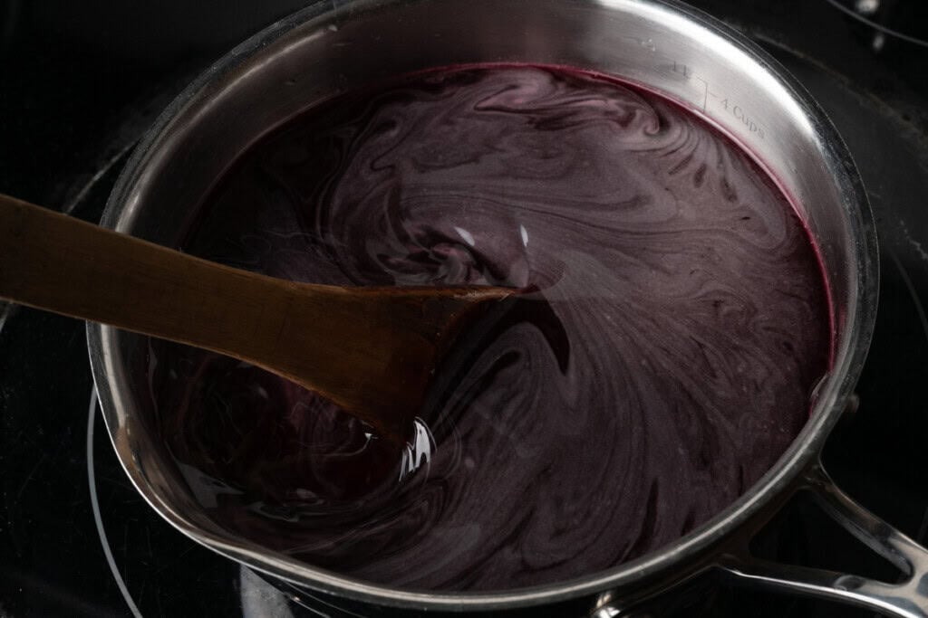 Stirring a pot of pomegranate juice, sugar, and orange blossom water with a wooden spoon